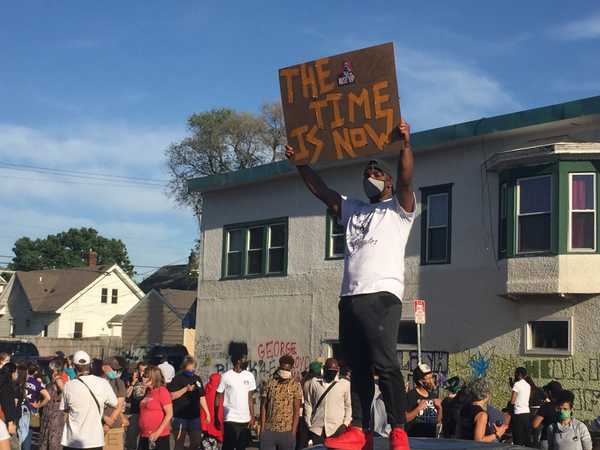 A black activist raises a sign reading, “THE TIME IS NOW” at George Floyd Memorial, Minneapolis, 3 days after Floyd’s death